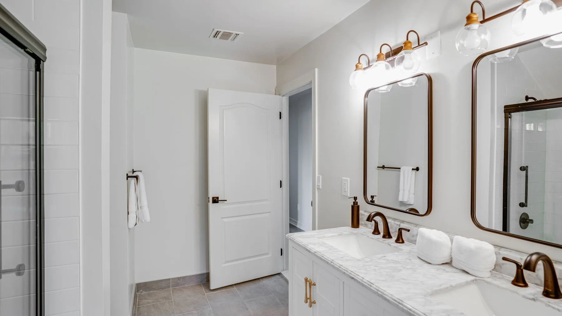 A bright bathroom with a long vanity, mirrors, and a glass shower.