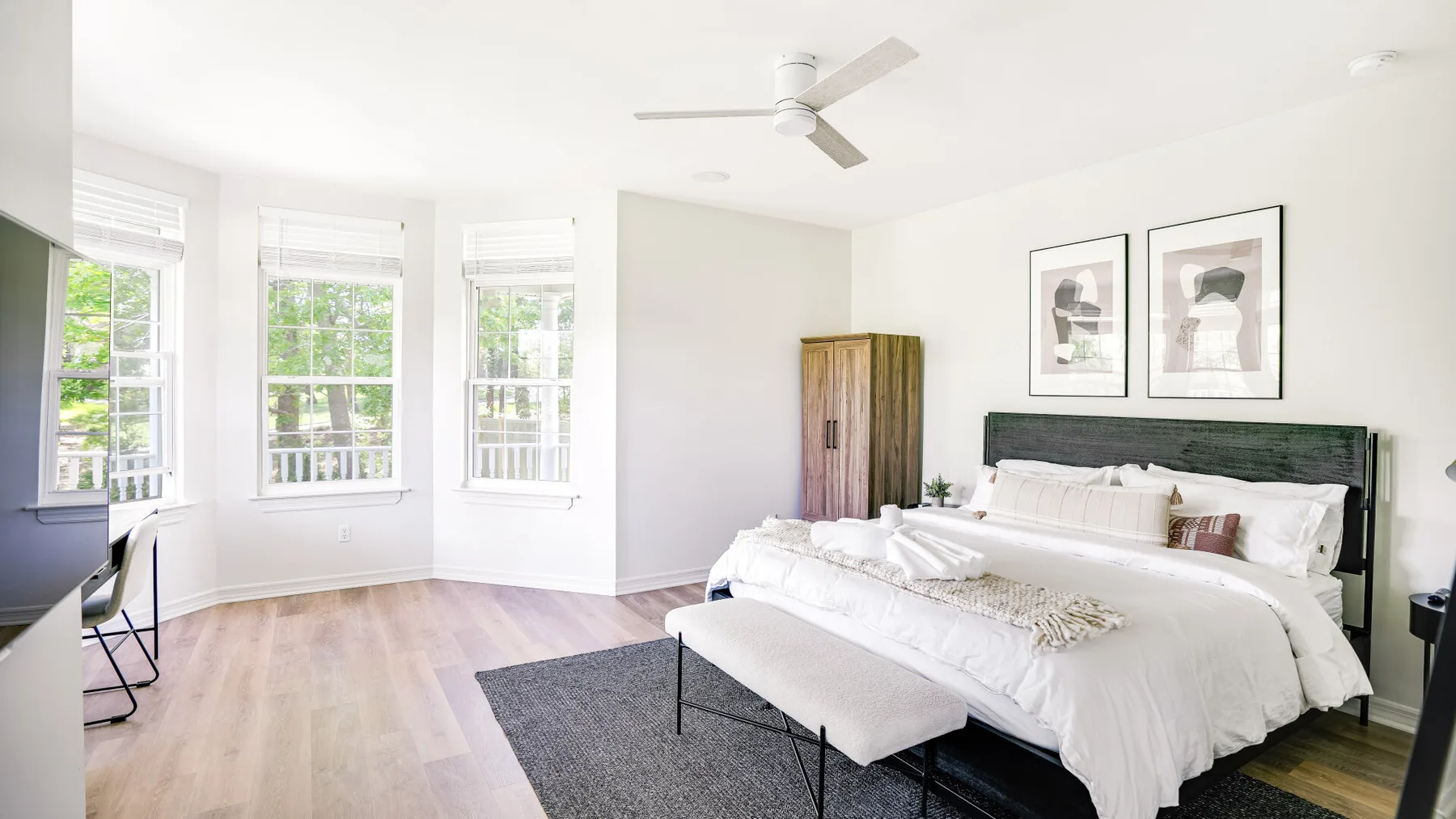 A bright bedroom with a large bed, an upholstered bench, and tall windows.