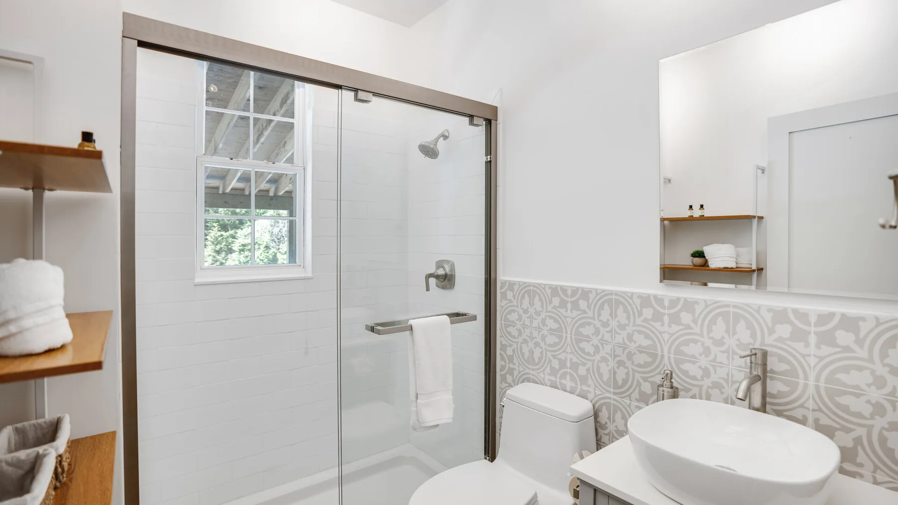 A bright bathroom with a glass shower, patterned tile, and a vessel sink.