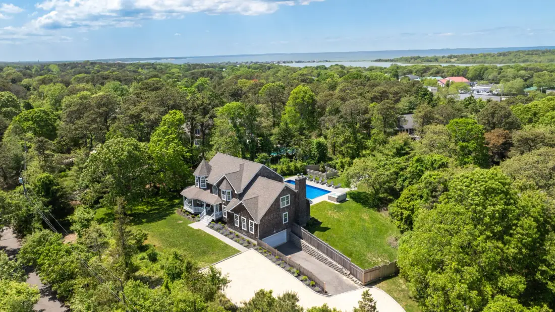 A large house sits amid green trees, with a pool beside it.