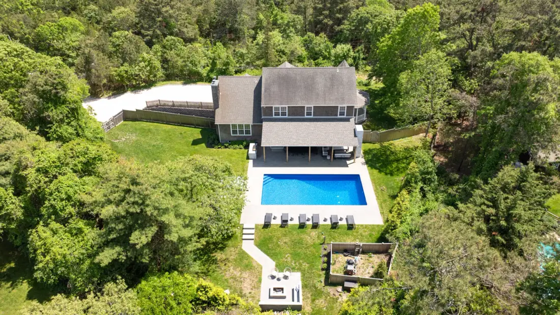 Aerial view of a house with a swimming pool surrounded by trees.