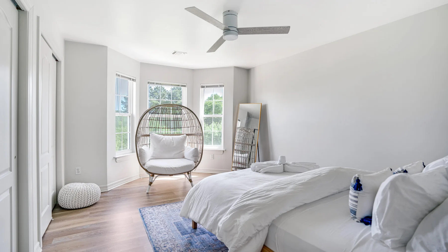 A bright bedroom with a bed, a hanging chair, and several windows.