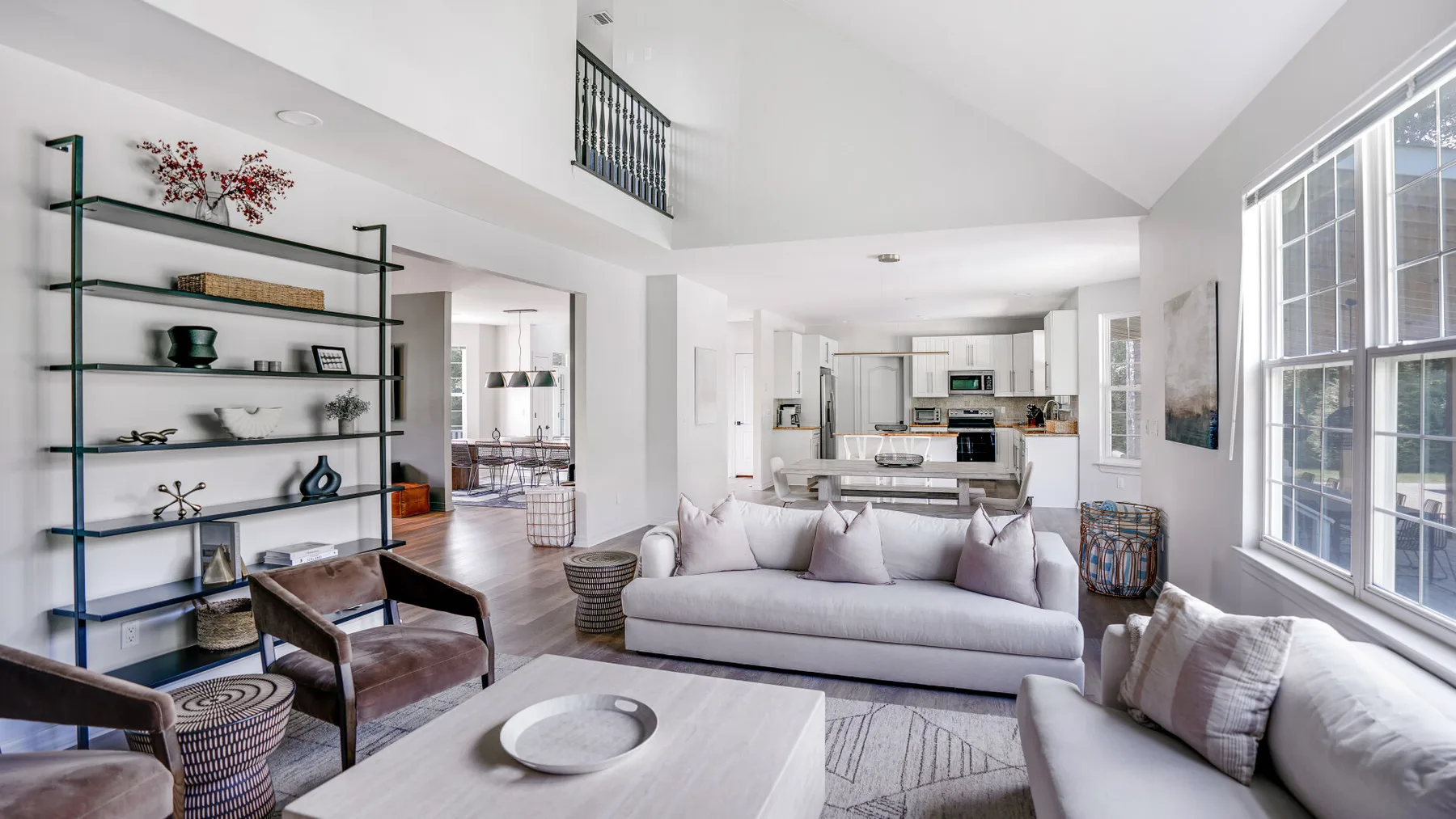 A bright living room with pale seating and an open kitchen in the background.