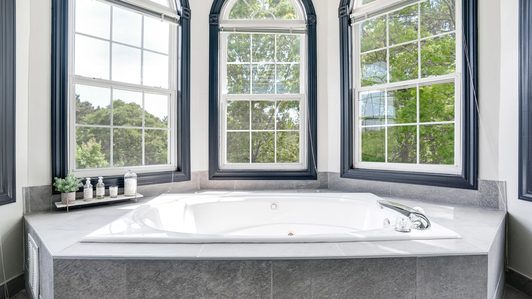 A built-in bathtub sits beneath three large windows.