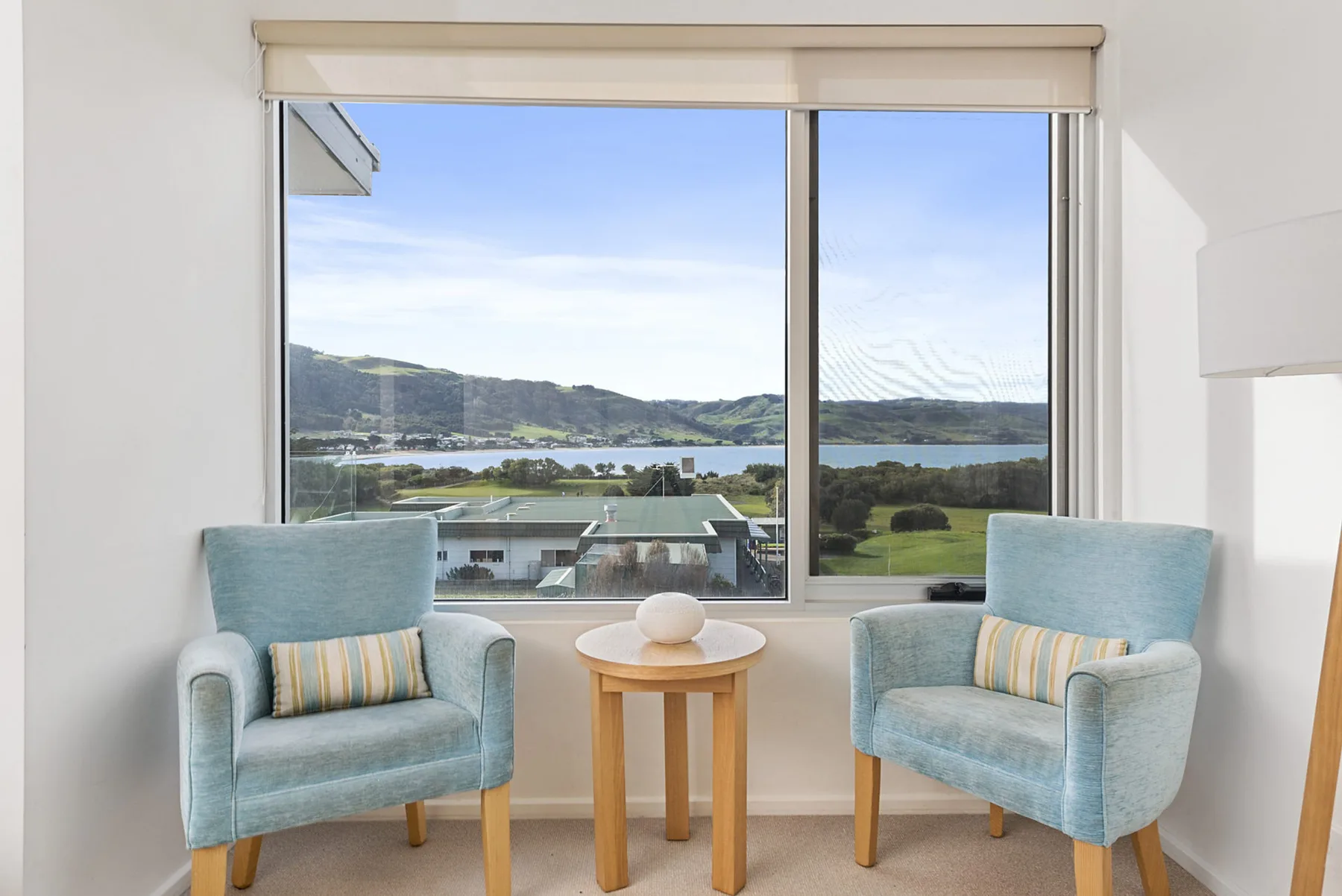 Una luminosa zona de estar tiene dos sillones junto a una ventana amplia con vistas al agua y las colinas.