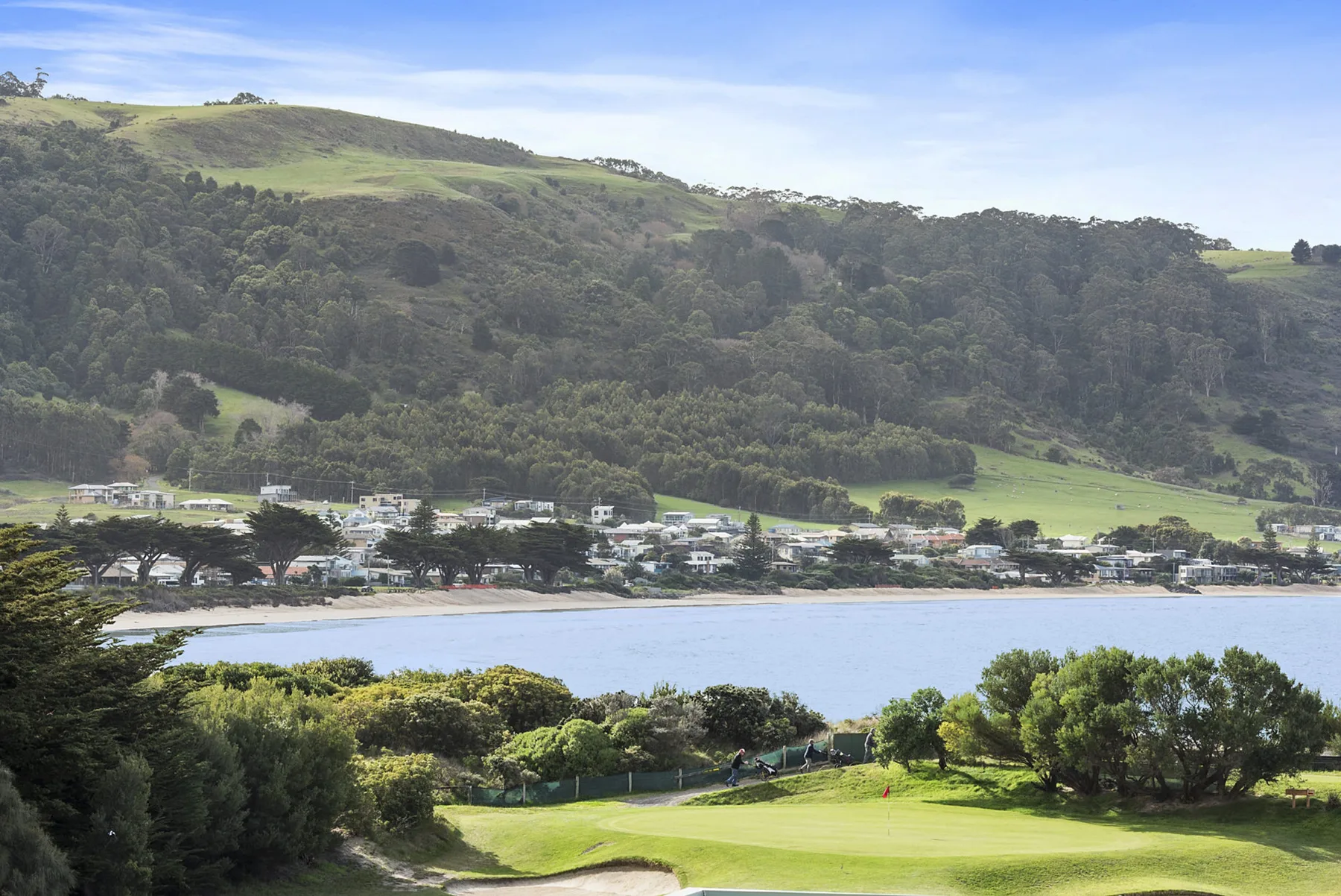 Paisaje costero con una bahía tranquila, colinas verdes y árboles.