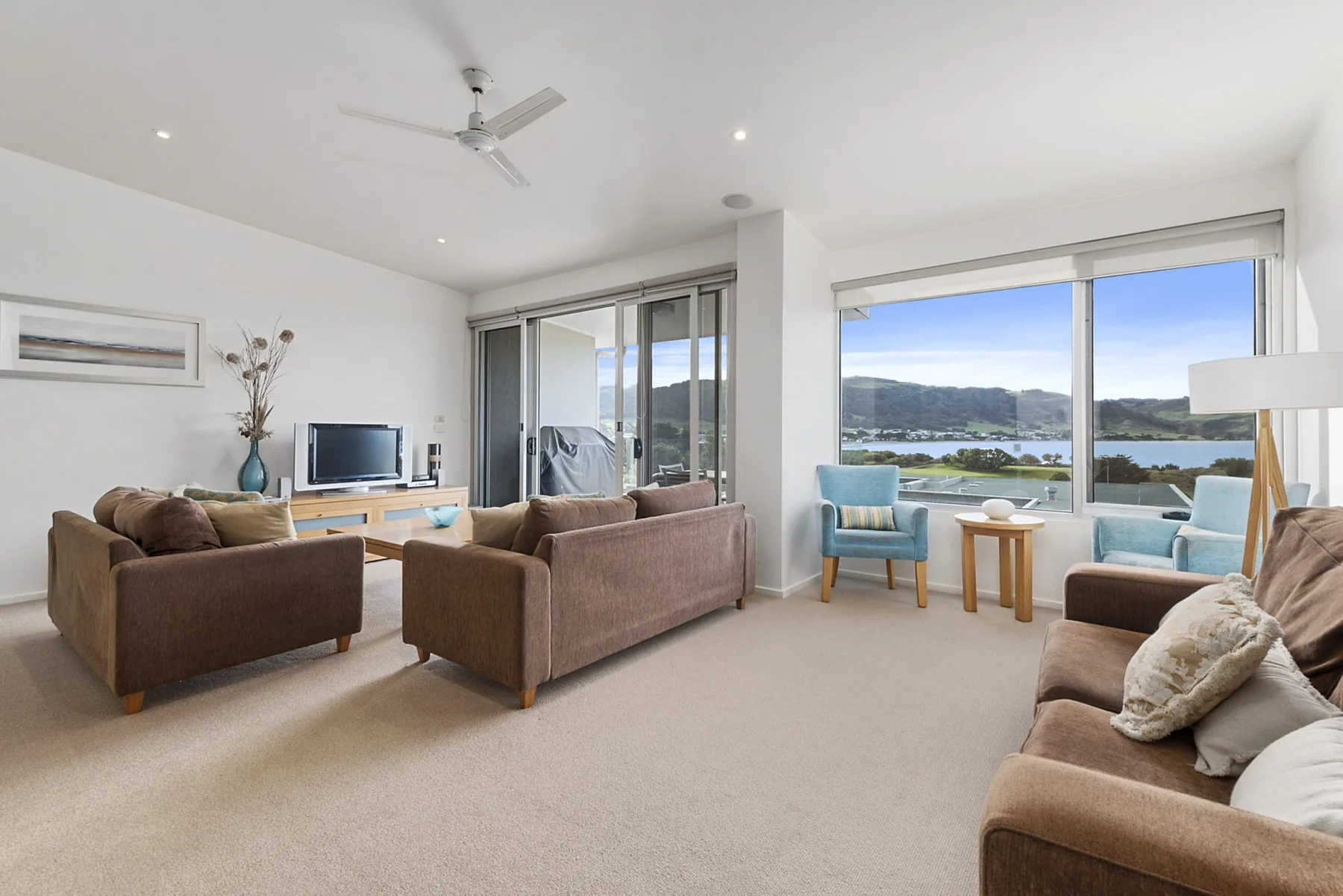 A bright living room with seating beside large windows overlooking the water.