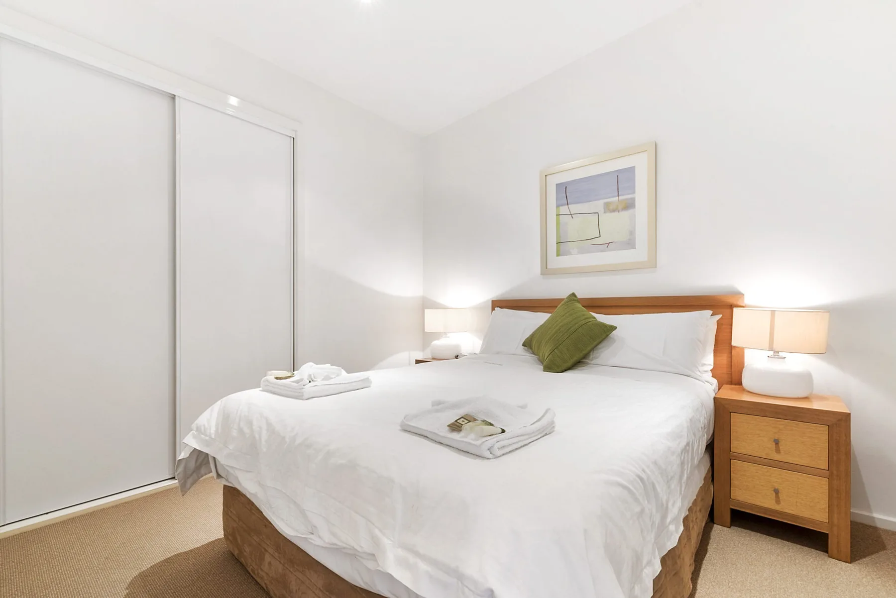 A bright bedroom with a neatly made bed and framed artwork above the headboard.