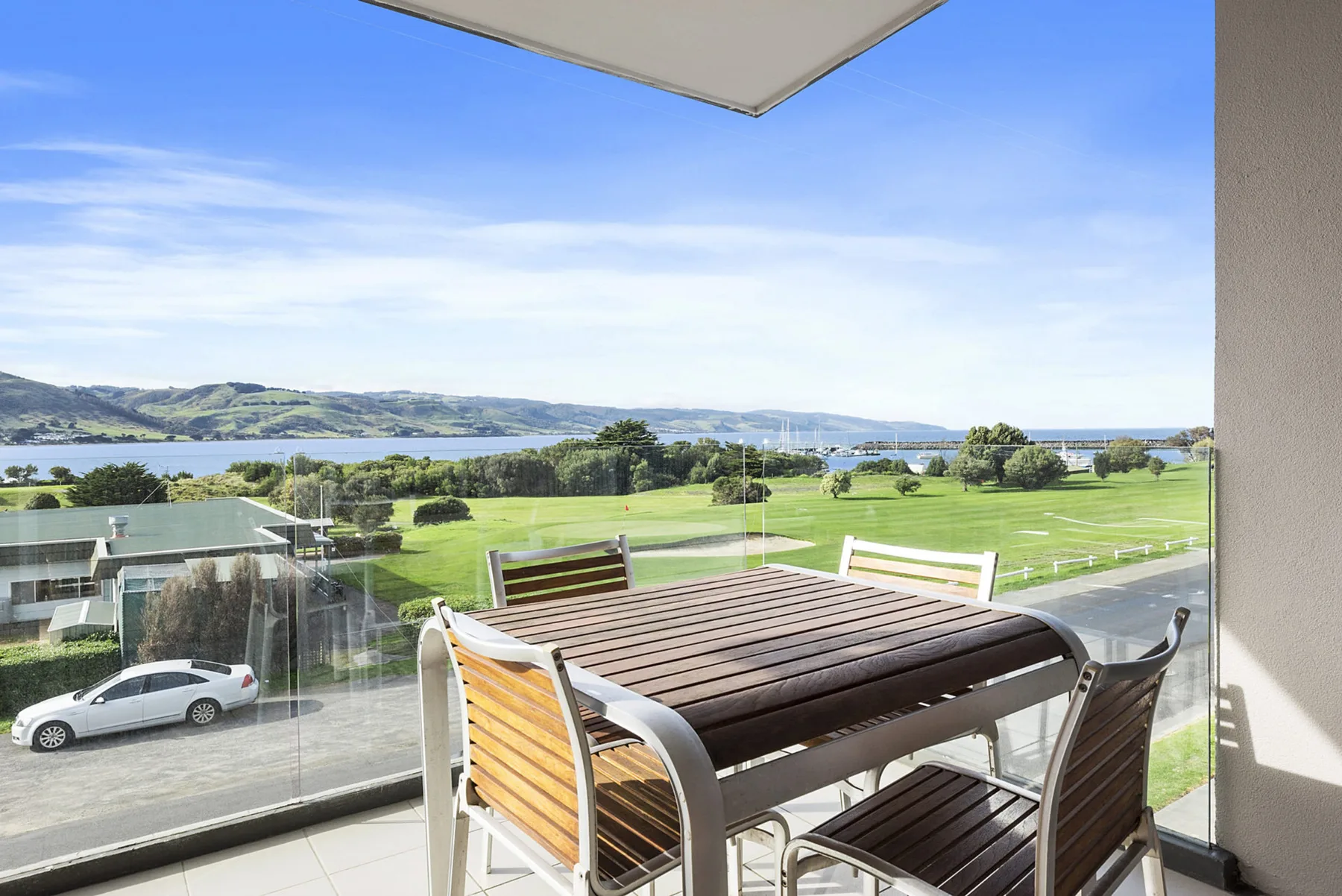 A balcony dining area overlooks a green park and the water.