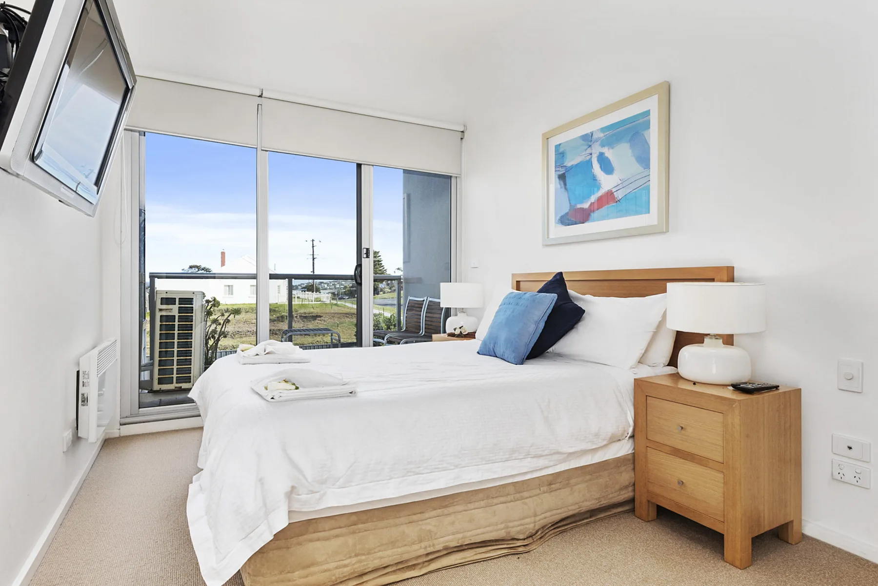 A bright bedroom with a neatly made bed beside large windows.