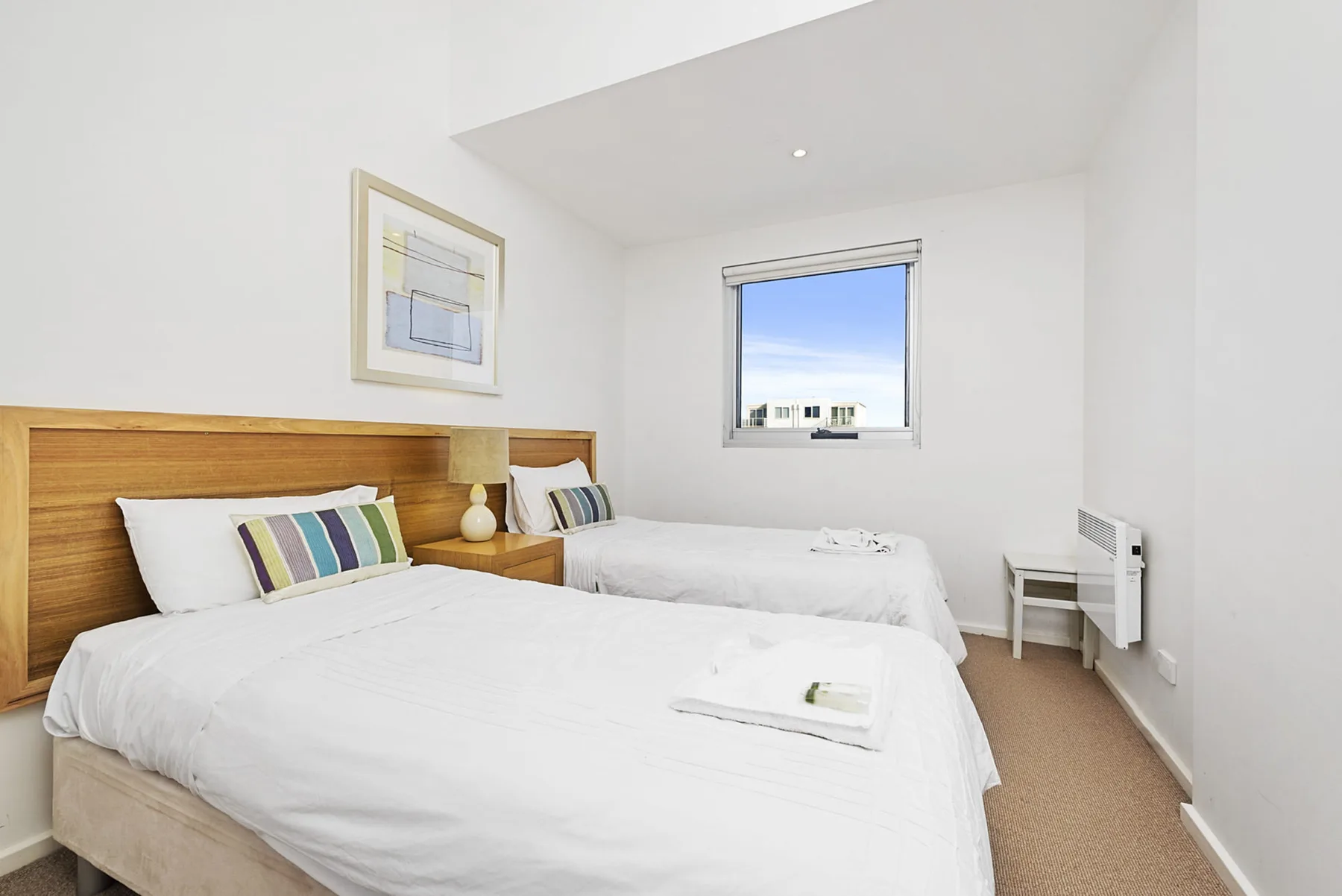 A bright bedroom with two beds and a window overlooking the sky.