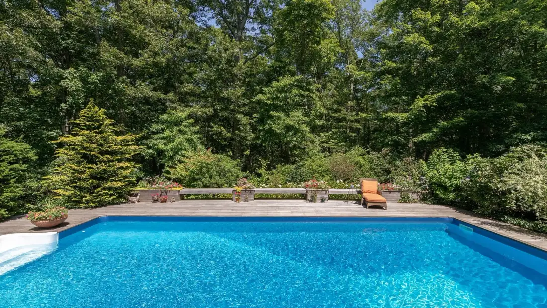 An outdoor swimming pool is bordered by a paved deck and trees.