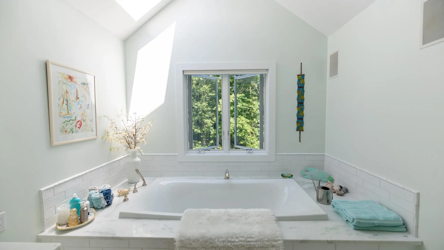 A bright bathroom features a built-in bathtub beneath a window overlooking greenery.