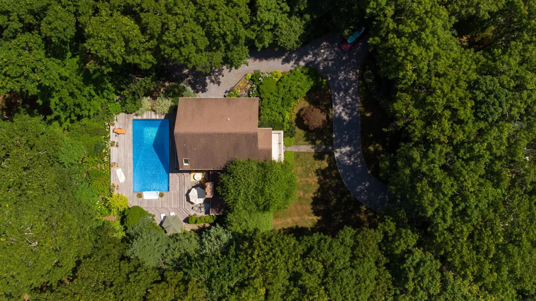 An aerial view of a house and swimming pool surrounded by dense greenery.