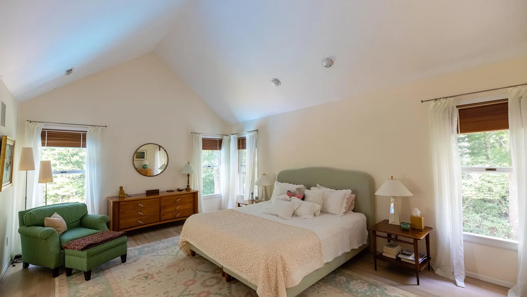 A bright bedroom with a bed, green seating, and windows overlooking greenery.