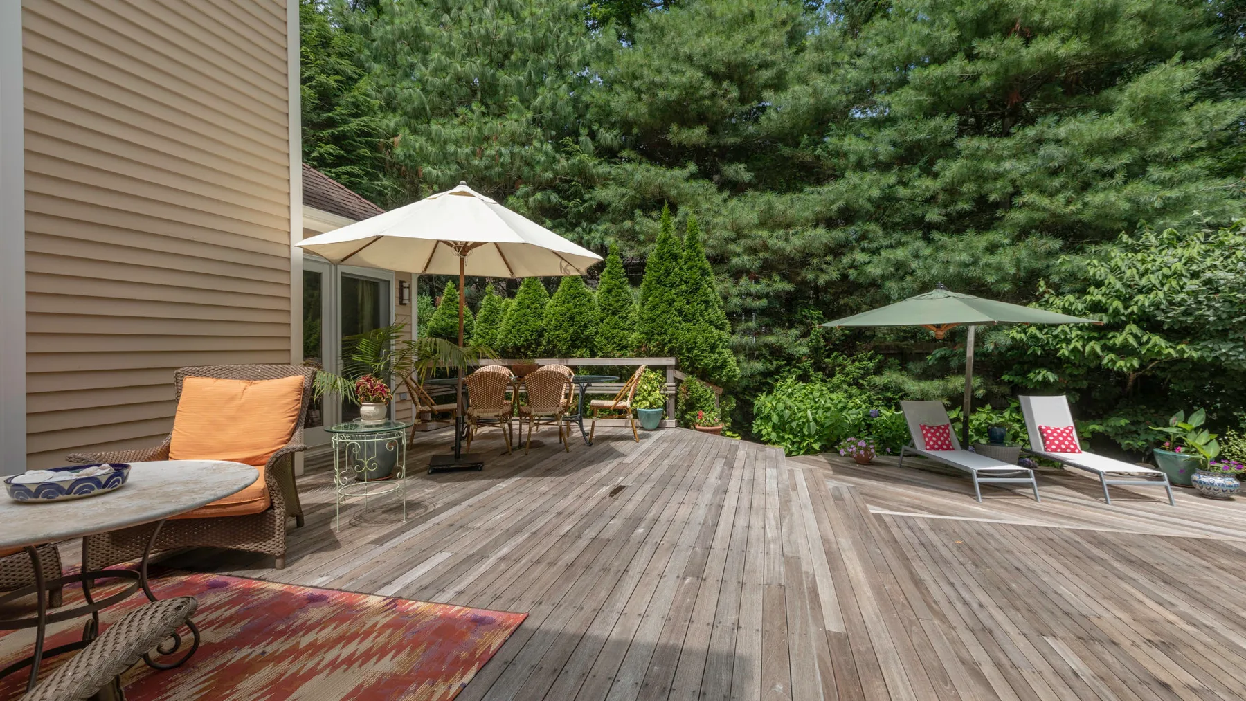 A wooden deck with outdoor seating, umbrellas, and trees surrounding the patio.