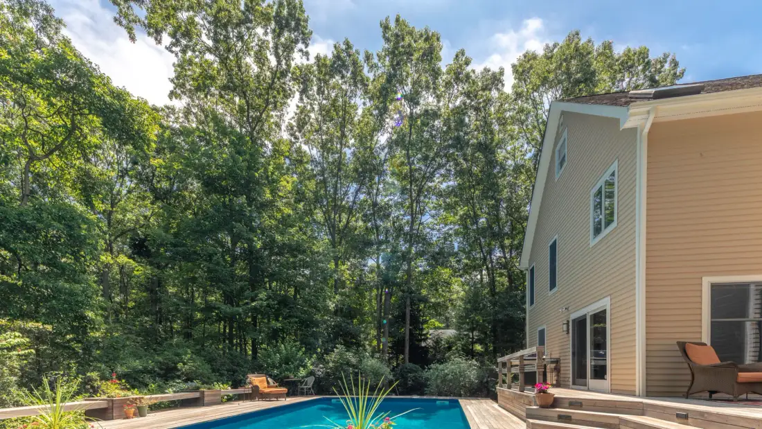 An outdoor pool beside a house, with trees surrounding the yard.