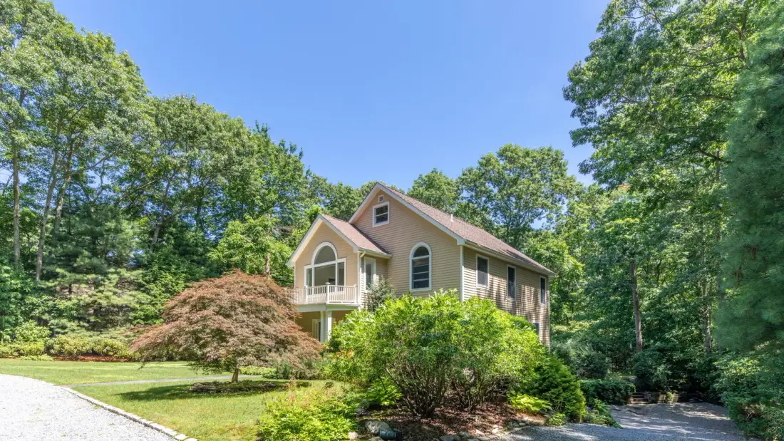 A house stands among trees and landscaped shrubs beside a curving driveway.