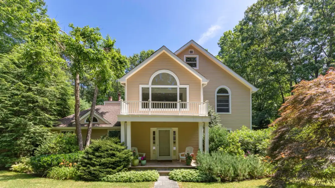 A house with a balcony and front garden surrounded by trees.
