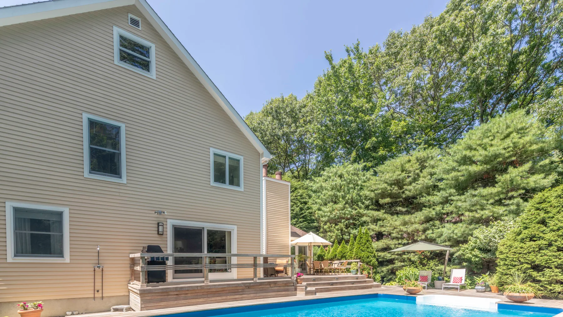 A house exterior with a wooden deck and a swimming pool among trees.