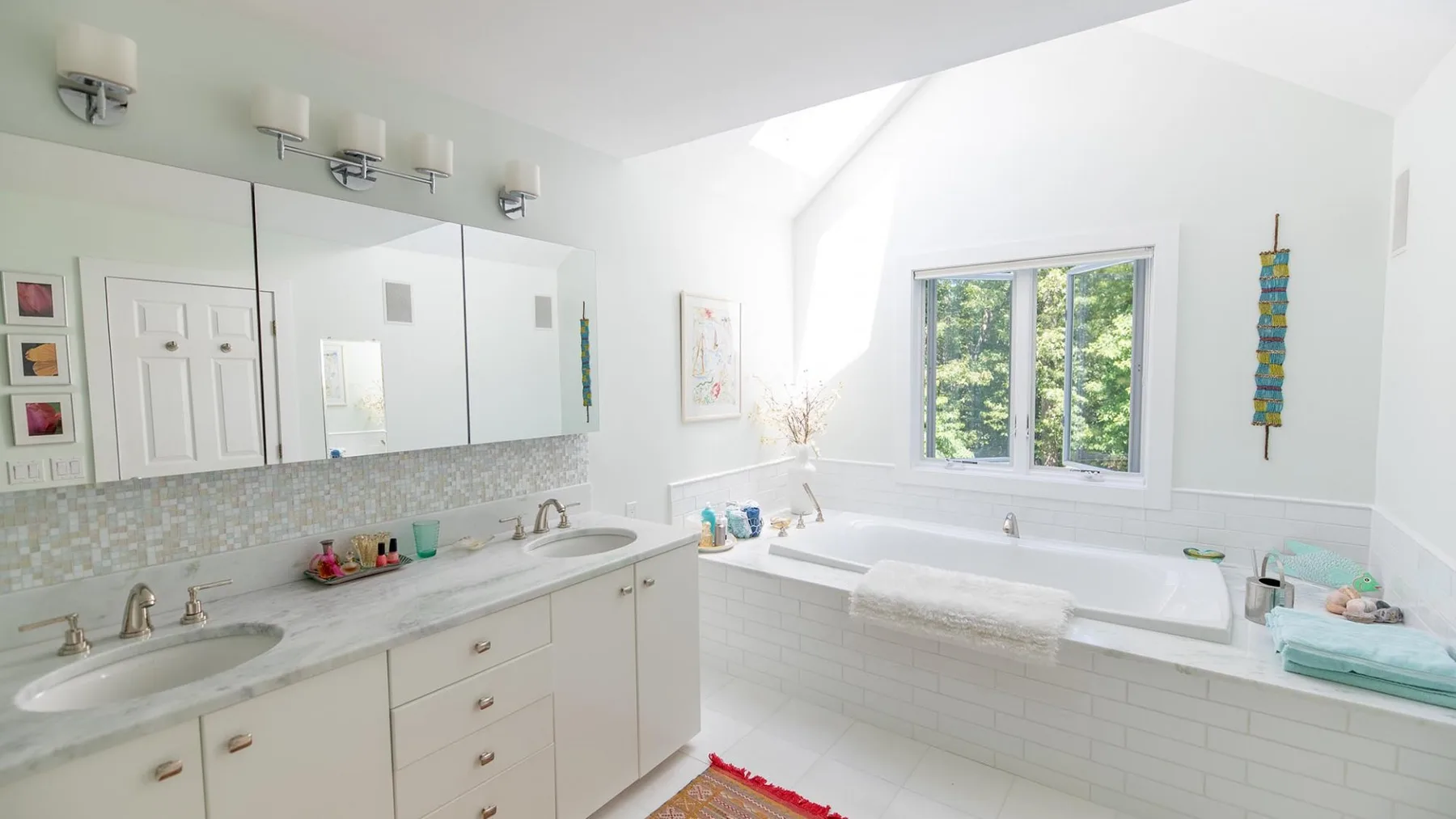 A bright bathroom with a long vanity and a bathtub beneath a window.