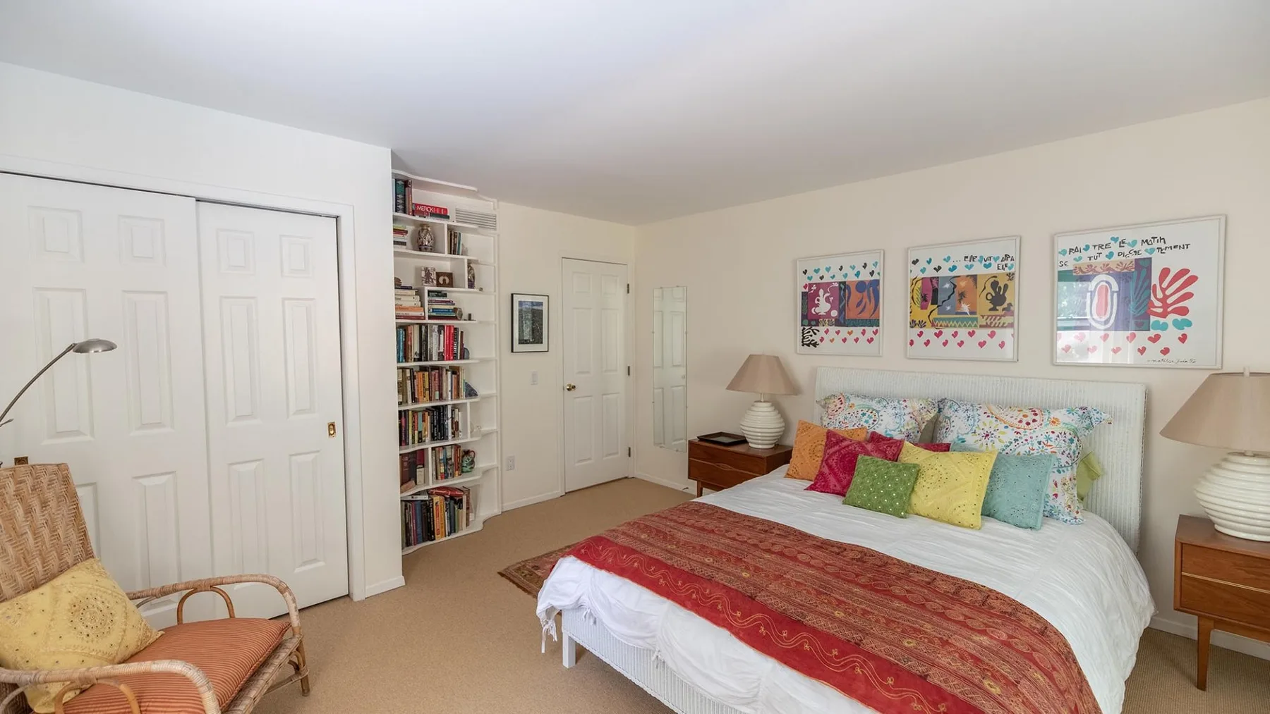 A bedroom with a bed, colorful pillows, and framed artwork above the headboard.
