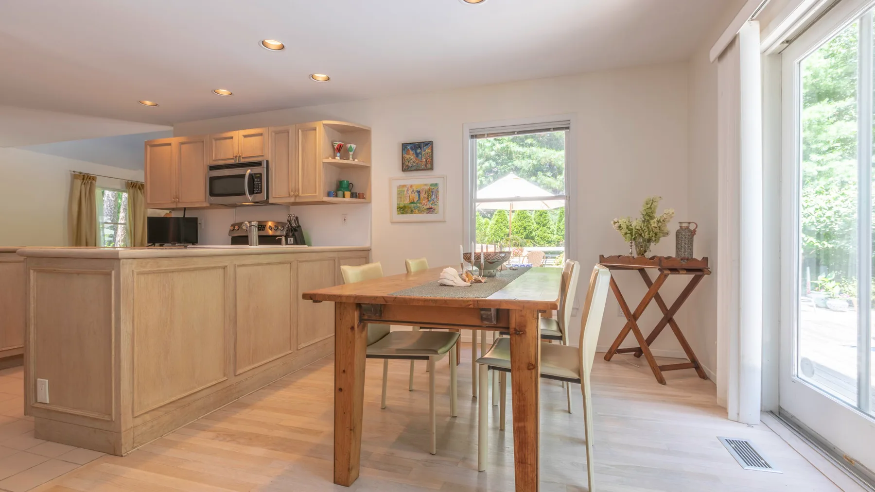 A bright kitchen and dining area with a wooden table beside large windows.