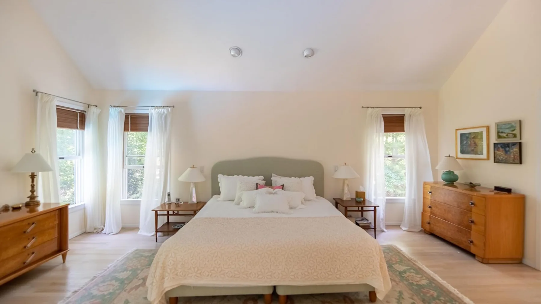 A bedroom with a bed, bedside tables, and windows dressed with curtains.