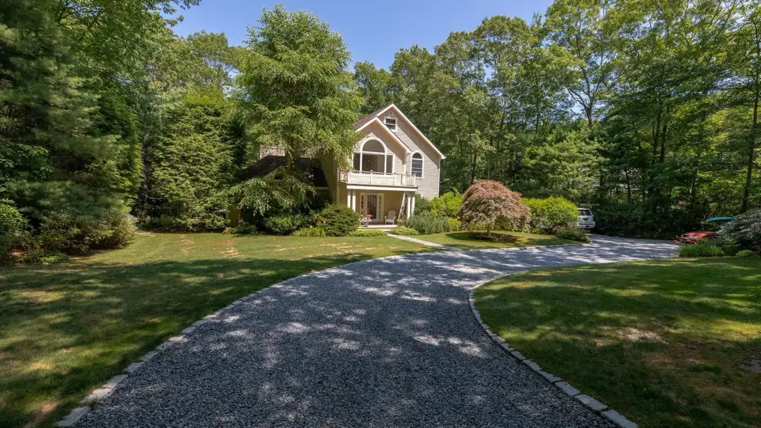 A house stands among trees beside a curving gravel driveway.
