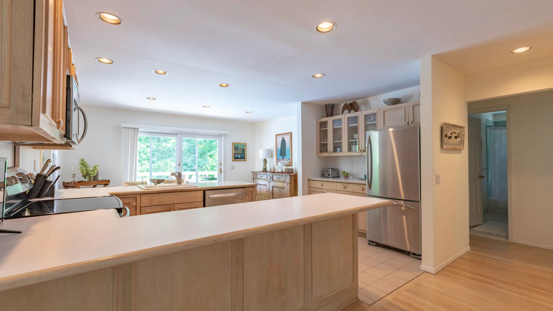 A bright kitchen with a long central island and stainless steel refrigerator.