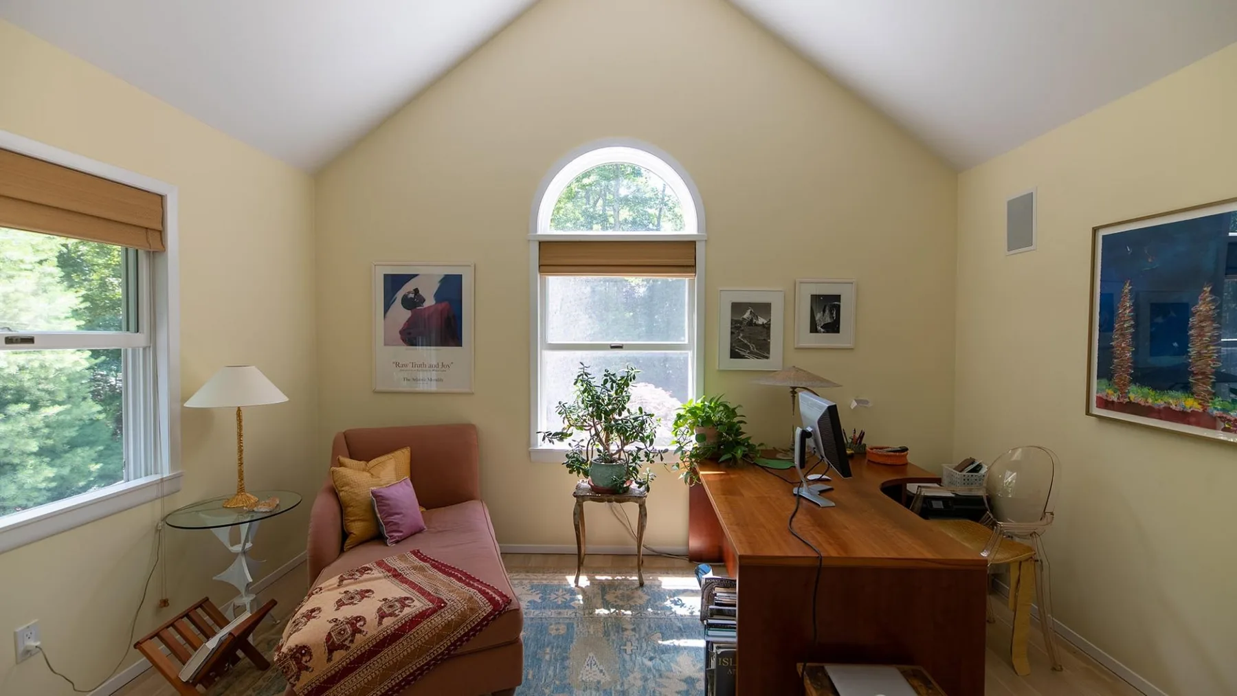 A bright room with a desk, seating, and windows overlooking greenery.
