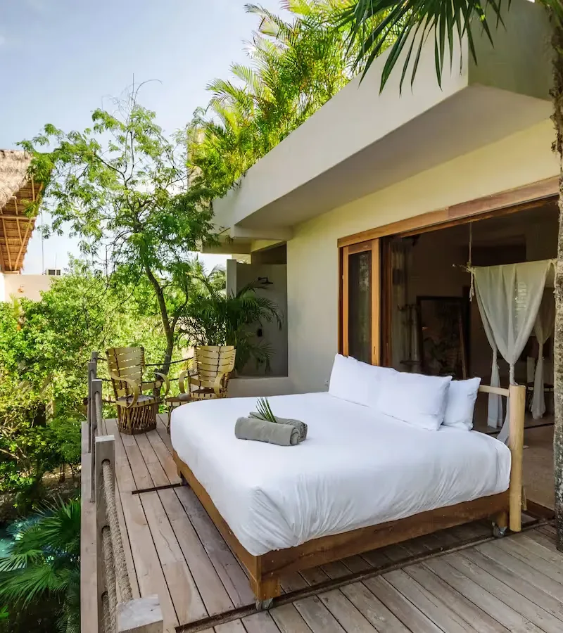 Outdoor bed on a wooden deck surrounded by tropical greenery.