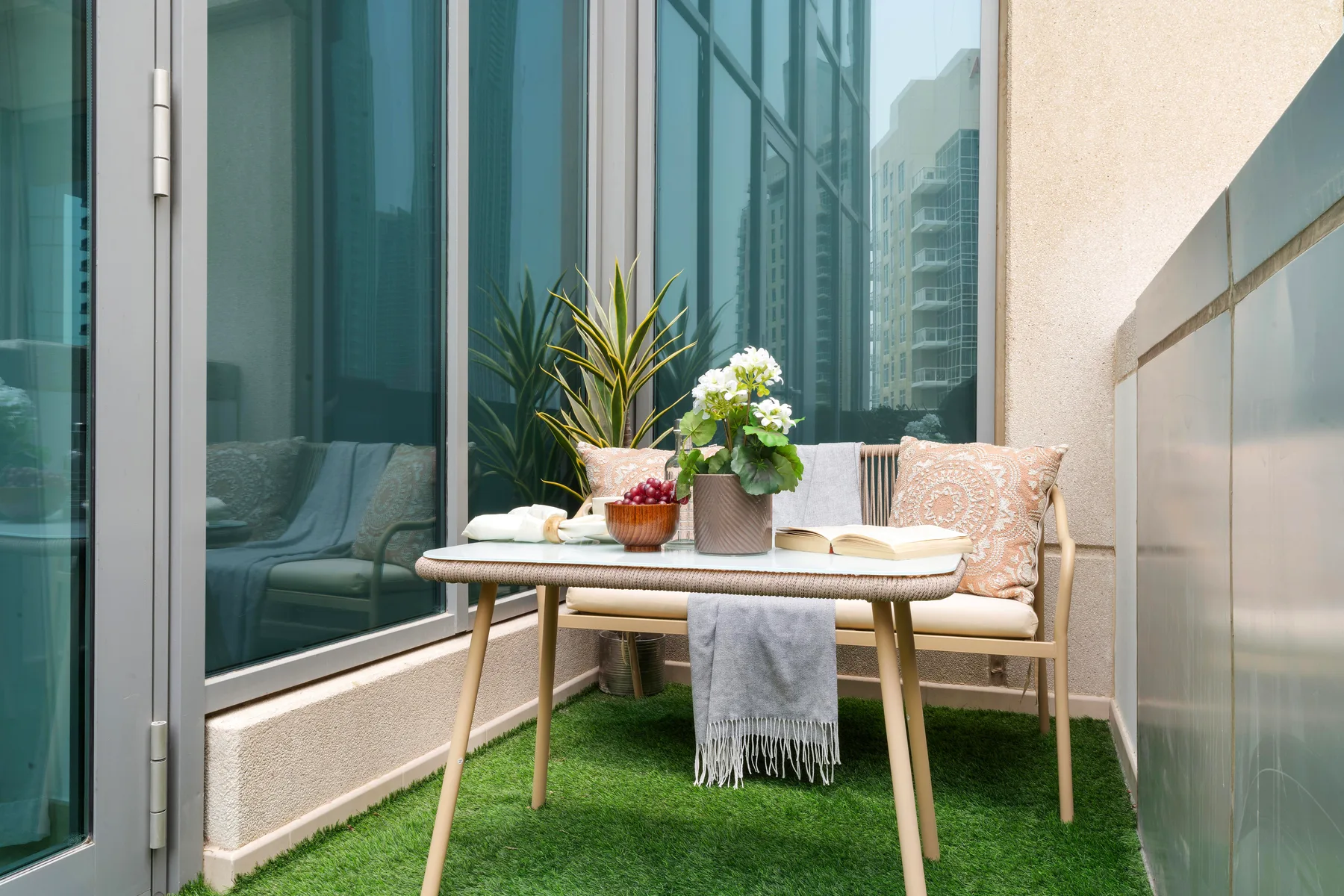 Una pequeña zona de estar en un balcón tiene una mesa con plantas en macetas y cojines.