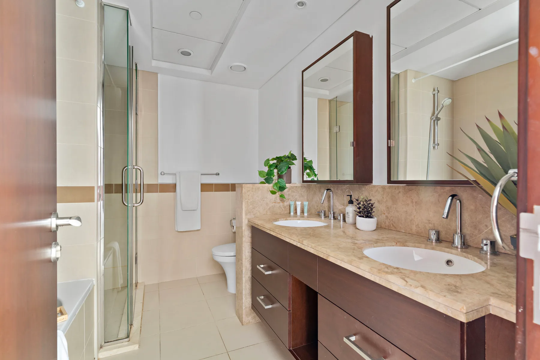 Un baño luminoso con una ducha de vidrio y un largo tocador con lavabo.