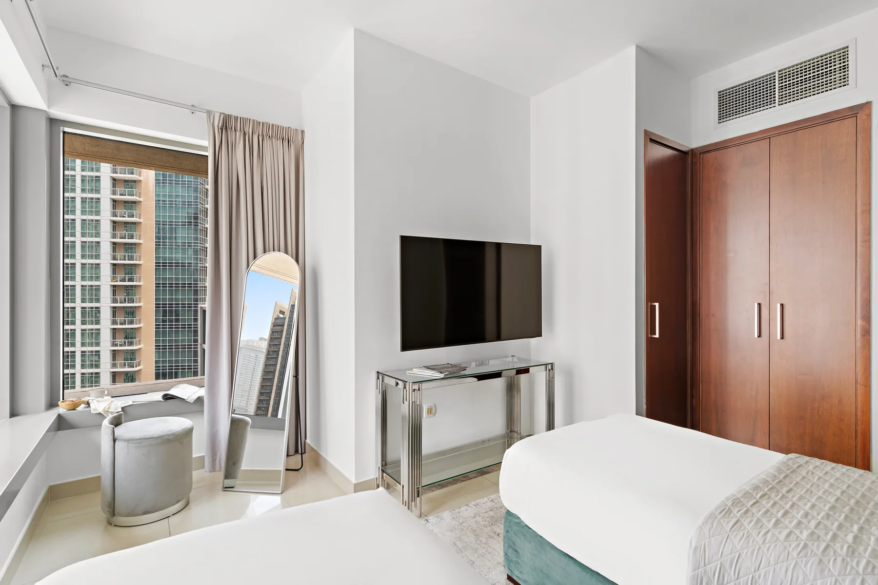 Un dormitorio luminoso con un televisor sobre un mueble junto a la ventana.