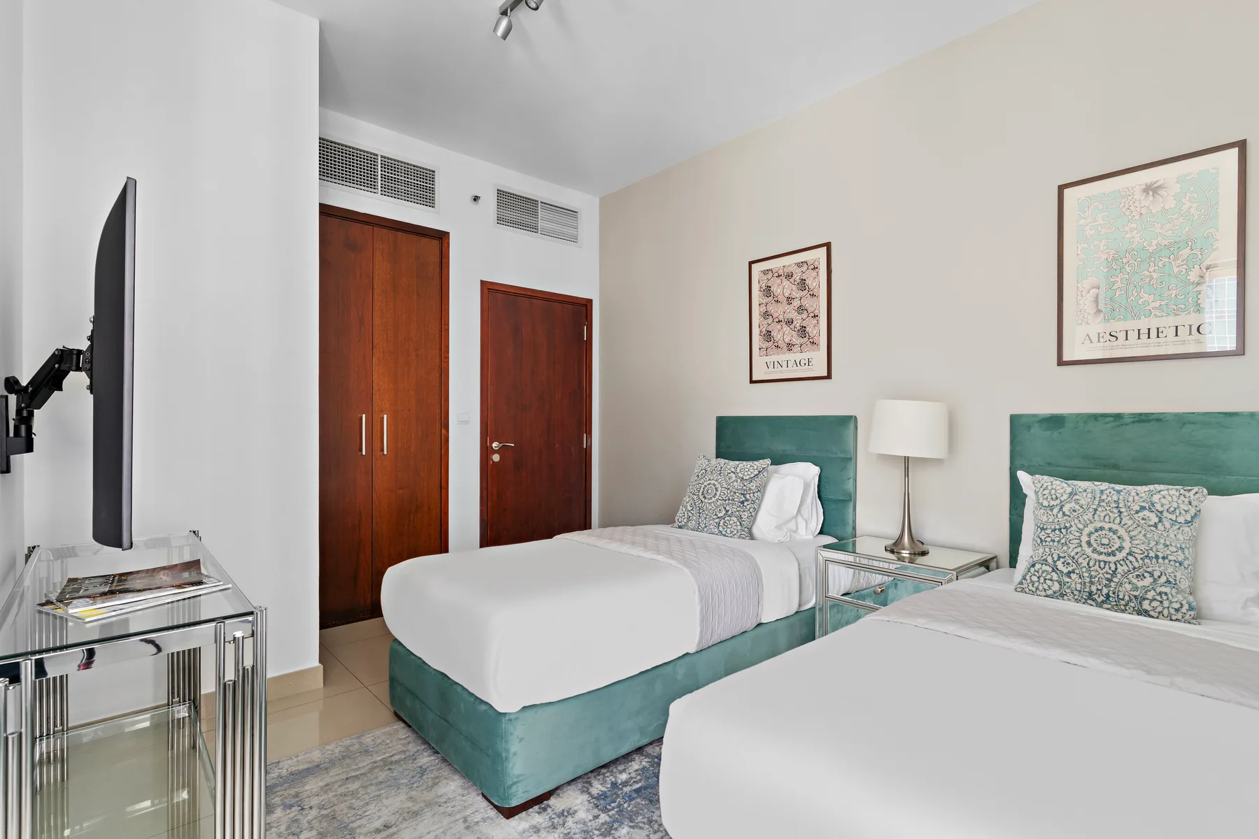 Un dormitorio con dos camas, cabeceros color turquesa y cuadros enmarcados.