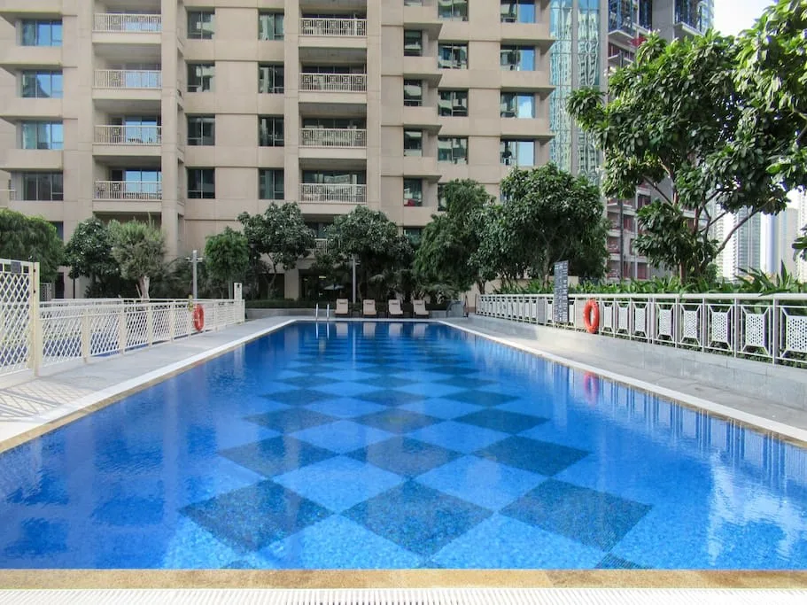 Una piscina al aire libre junto a un edificio residencial y árboles frondosos.