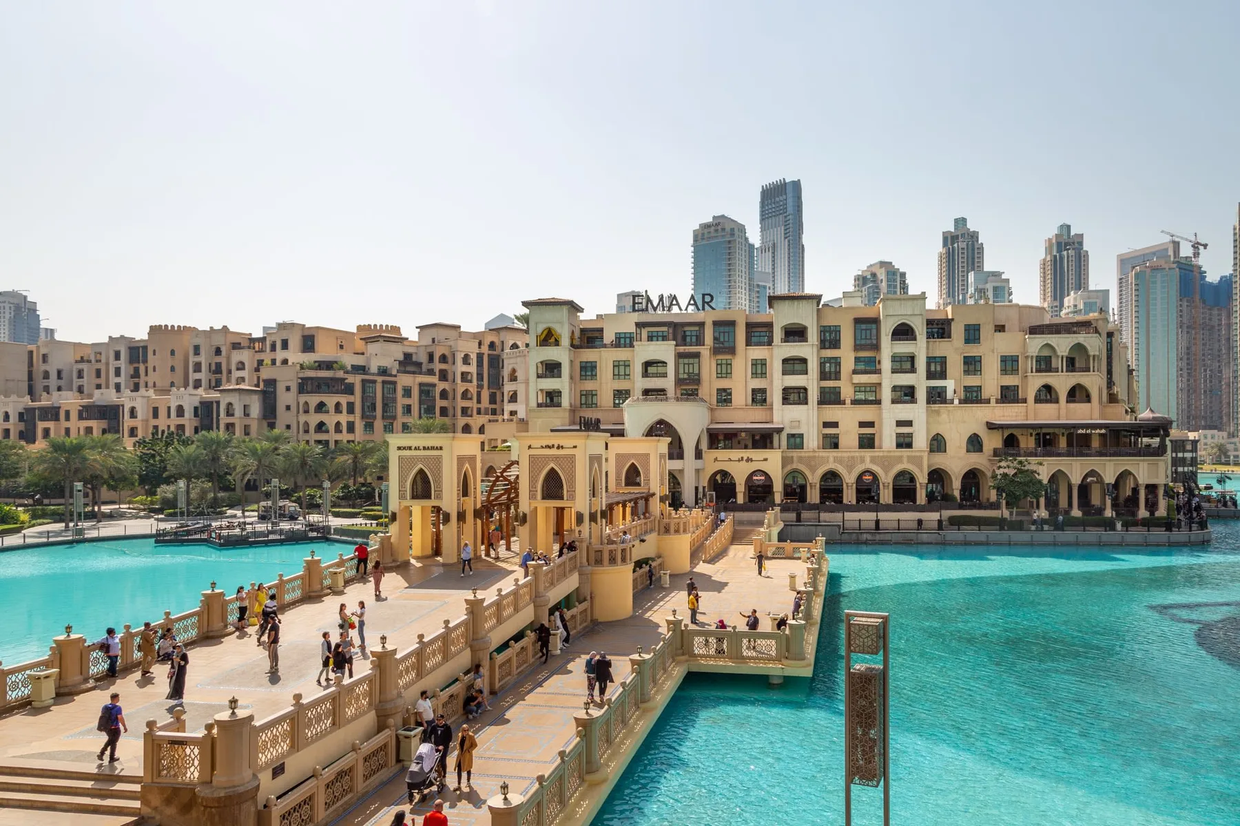 Un complejo hotelero frente al agua da a una piscina turquesa, con un puente peatonal delante.