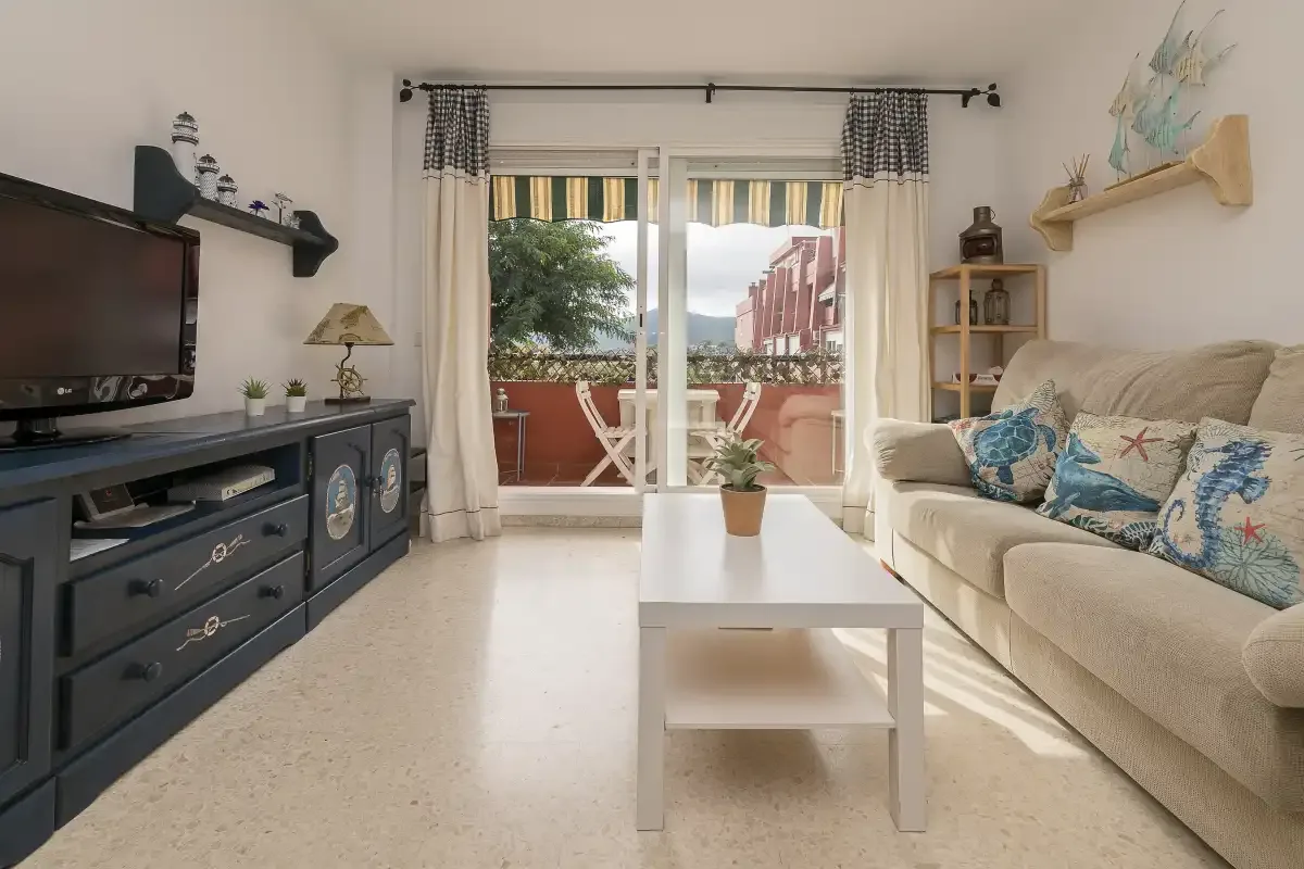 Living room with a television, seating, and a coffee table beside balcony doors.