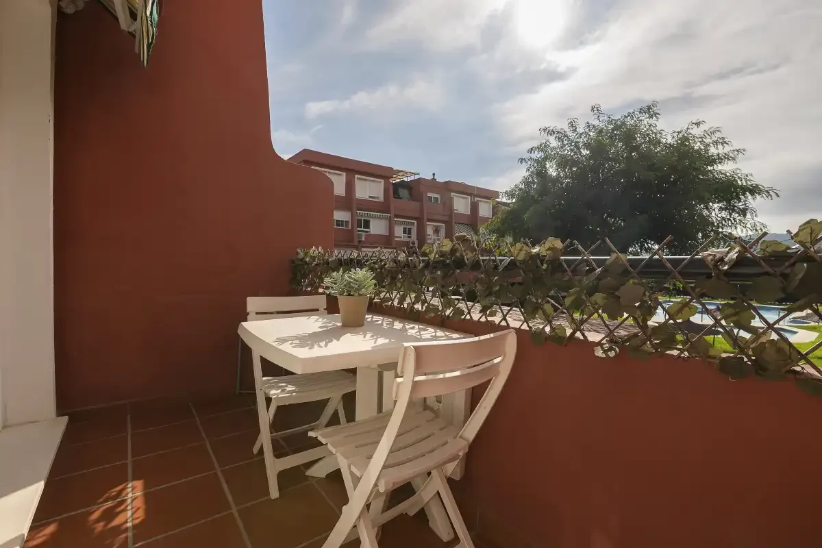 A small outdoor patio has a white table and chairs beside a red wall.