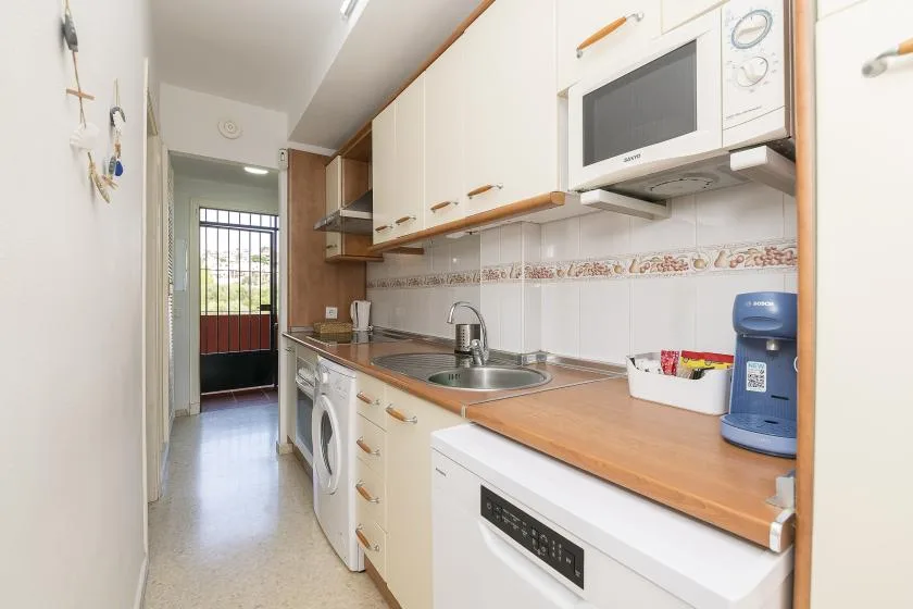 A narrow kitchen with a long countertop, sink, and built-in appliances.