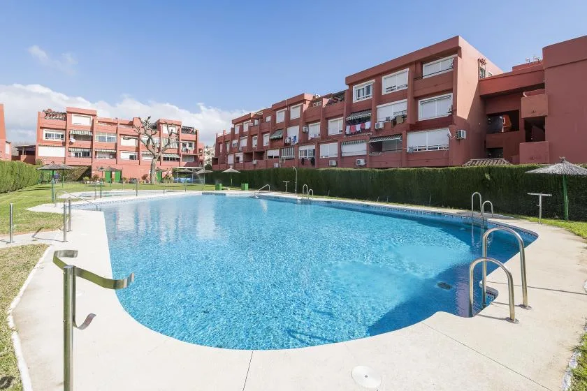 An outdoor swimming pool sits beside a paved deck and residential buildings.