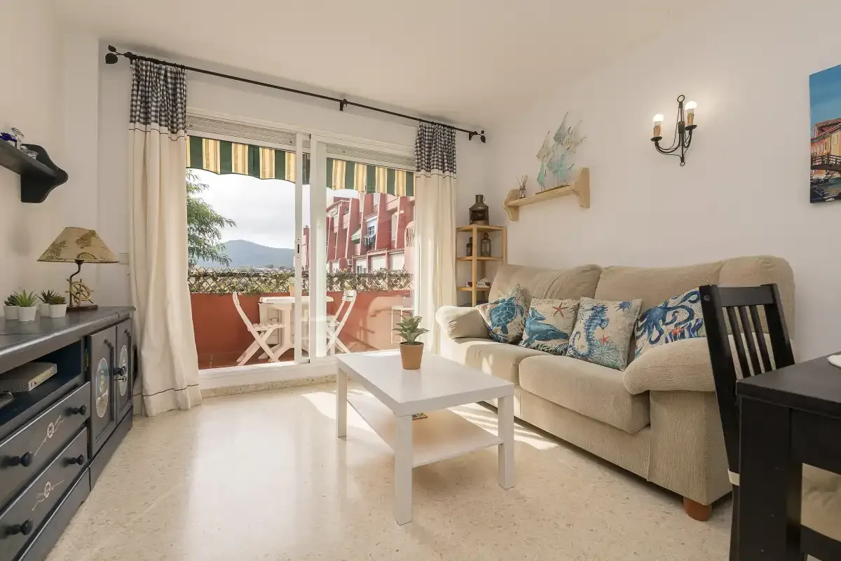 A bright living room with seating and a coffee table beside glass doors opening to a balcony.