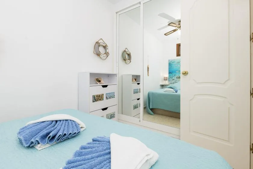 A bedroom with a neatly made bed and folded towels beside mirrored closet doors.