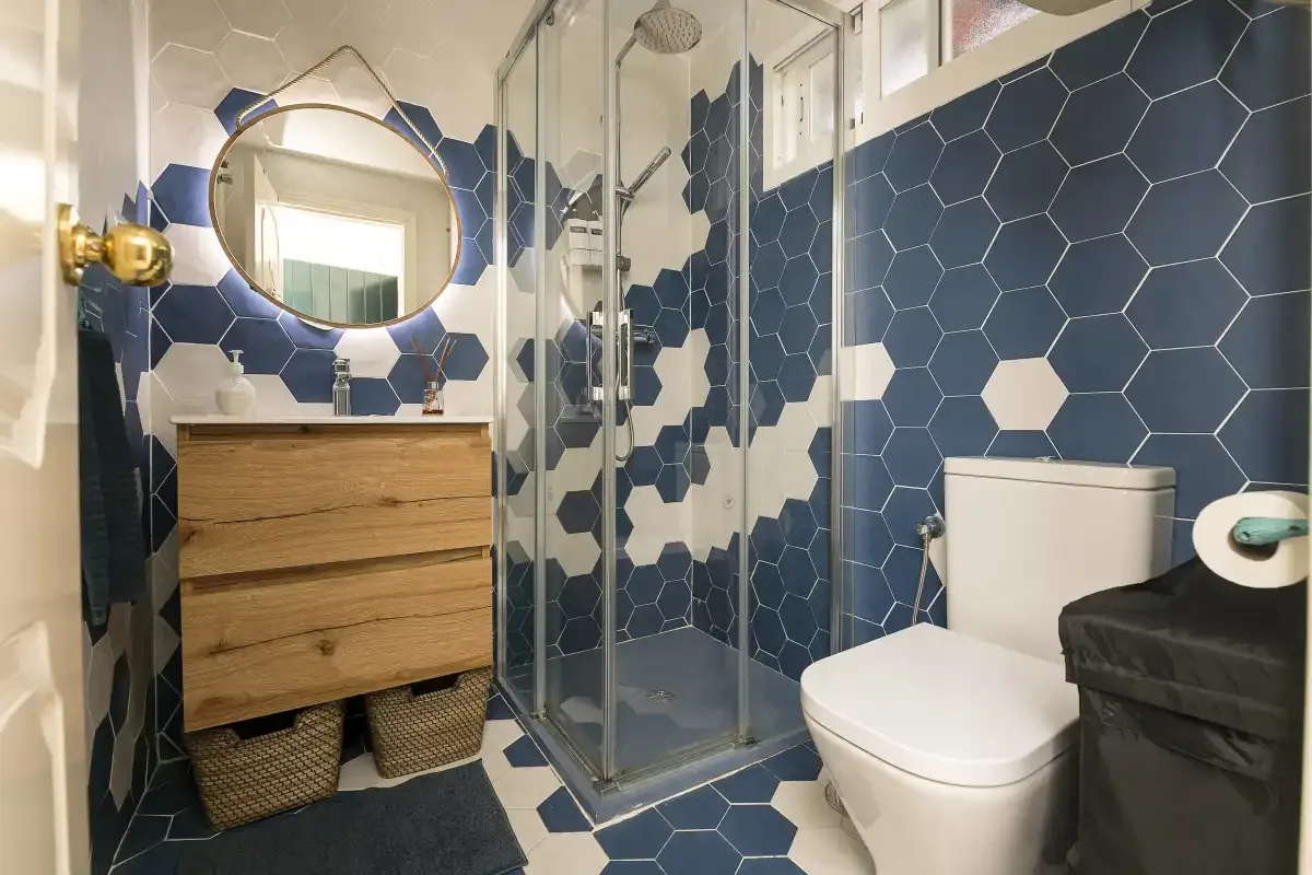 A bathroom with a glass shower, wood vanity, and blue-and-white tile.