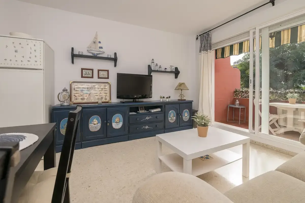 A living room with a television on a blue sideboard and a bright patio view.