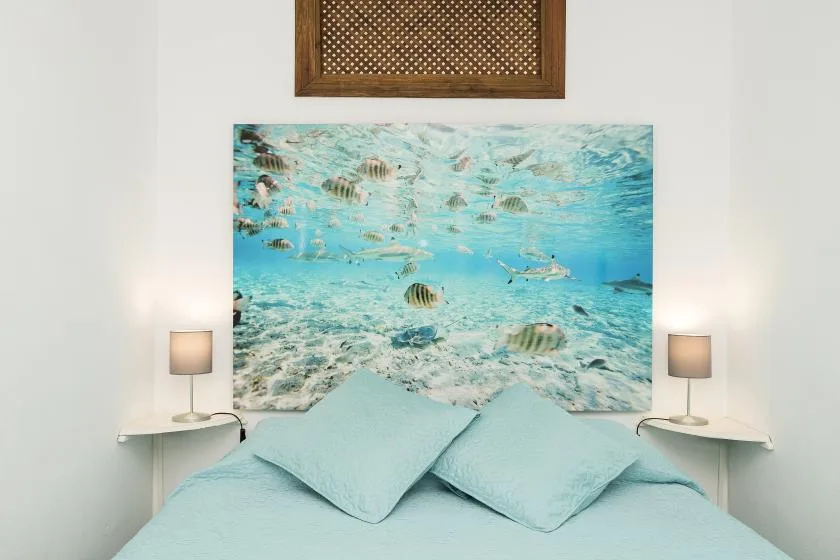 A bedroom with pale blue bedding beneath a large underwater-themed wall picture.