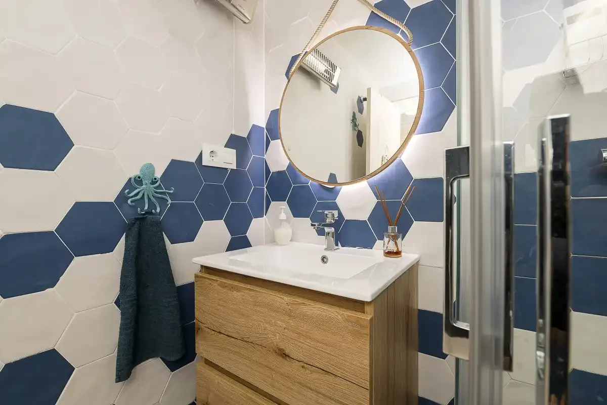 A bathroom vanity with a round mirror and blue-and-white tiled walls.