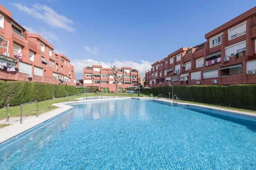 A swimming pool sits among red apartment buildings beneath a clear blue sky.