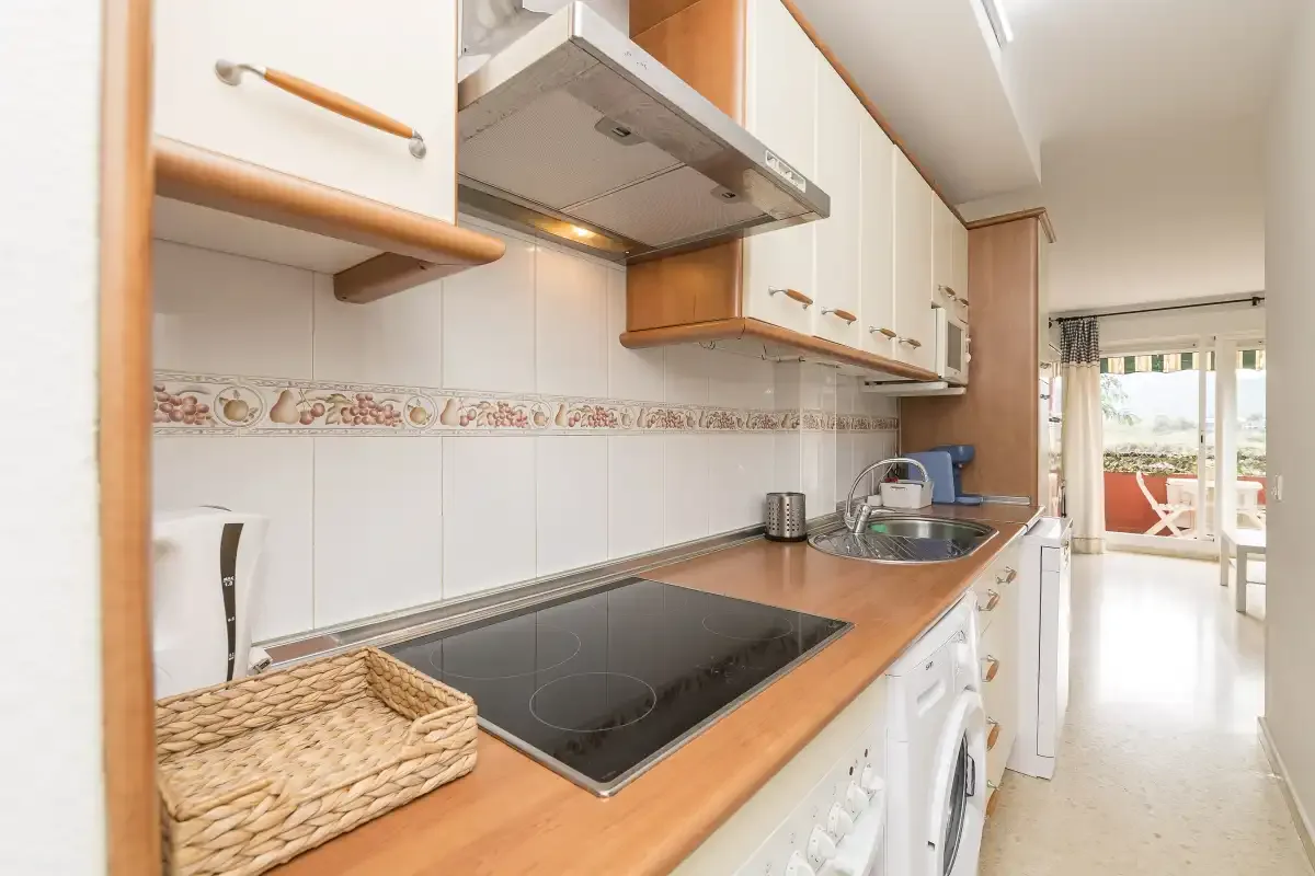 A compact kitchen with a cooktop and counter beside a bright glass door.